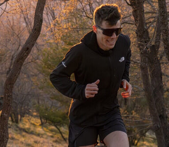 Male runner trail running through woods at sunset wearing affordable performance sports sunglasses