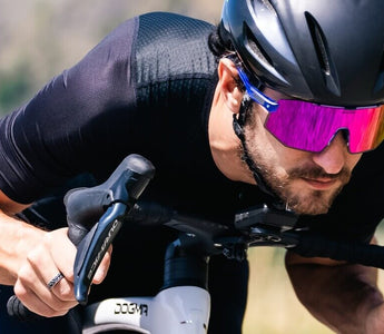 Male road cyclist riding a bike while wearing photochromic sports sunglasses with purple tint lenses