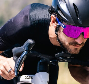 Male road cyclist riding a bike while wearing photochromic sports sunglasses with purple tint lenses