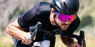 Male road cyclist riding a bike while wearing photochromic sports sunglasses with purple tint lenses